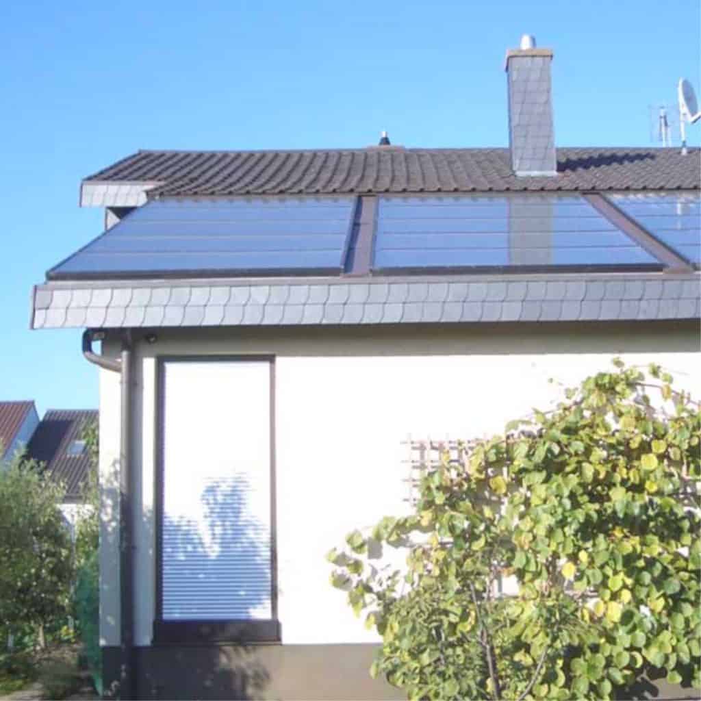 Seitliche Ansicht eines weißen Einfamilienhaus mit Solarmodulen auf dem Schrägdach. Grünanlage und blauer Himmel umranden das Haus